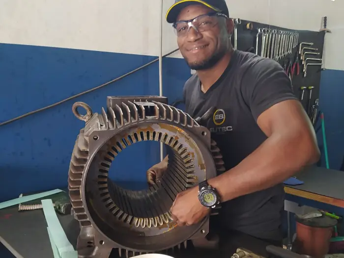 Técnico da Eutec Brasil com um estator de motor elétrico na bancada da oficina